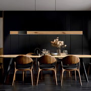 Moderne Pendelleuchte PURE-MOTO-RISE über einem Esstisch, aus Holz und Metall, in einem stilvollen Esszimmer mit dunklen Wänden, seitliche Perspektive.