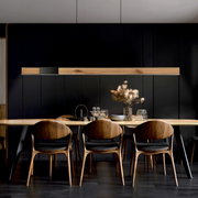 Moderne Pendelleuchte PURE-MOTO-RISE über einem Esstisch, aus Holz und Metall, in einem stilvollen Esszimmer mit dunklen Wänden, seitliche Perspektive.
