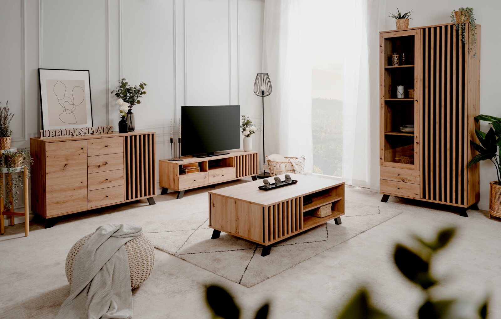 Modernes Wohnzimmer-Set aus hellem Holz mit Sideboard, TV-Lowboard, Couchtisch und Vitrine mit vertikalen Lamellen und schwarzen Füßen; aufgenommen in leichter Schrägansicht von vorn.