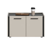 Modernes Lowboard/Sideboard mit zwei hellen Fronttüren und schwarzen Griffleisten, dunkler Ablagefläche und seitlichem Rahmen, darauf Becher und braunes Etui, Ansicht von vorne mit leicht erhöhter Perspektive.