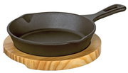 Gusseiserne Grillpfanne mit Holzgriff auf einem runden Holzbrett, seitliche Perspektive