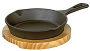 Gusseiserne Grillpfanne mit Holzgriff auf einem runden Holzbrett, seitliche Perspektive