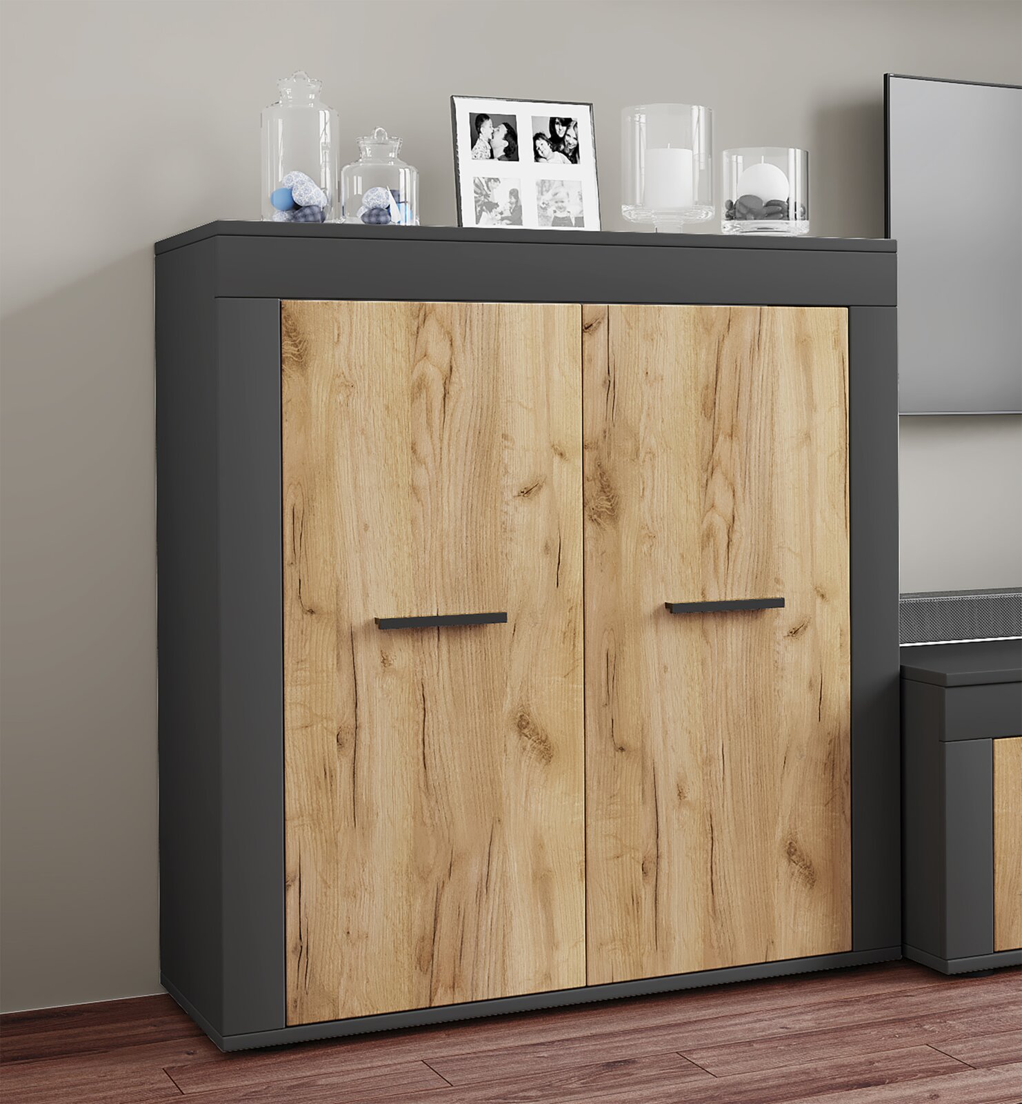Zweitüriges Sideboard in Anthrazit mit Holzoptik-Fronten und schwarzen Griffen, frontal aus leicht schräger Perspektive im Wohnraum inszeniert
