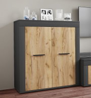 Zweitüriges Sideboard in Anthrazit mit Holzoptik-Fronten und schwarzen Griffen, frontal aus leicht schräger Perspektive im Wohnraum inszeniert