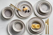 Vogelperspektive auf ein 12-teiliges Tellerset mit grauem, gesprenkeltem Design, bestehend aus Tellern und Schalen, dekoriert mit goldfarbenem Besteck und Lebensmitteln.