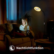 Schwarze LED-Stehlampe mit rundem Leuchtenkopf und warmem Nachtlicht, seitliche Ansicht im Wohnzimmer neben einem Sofa