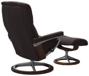 Achterkant van een bruine fauteuil met bijpassende voetenbank, beide met een modern frame van metaal en hout.