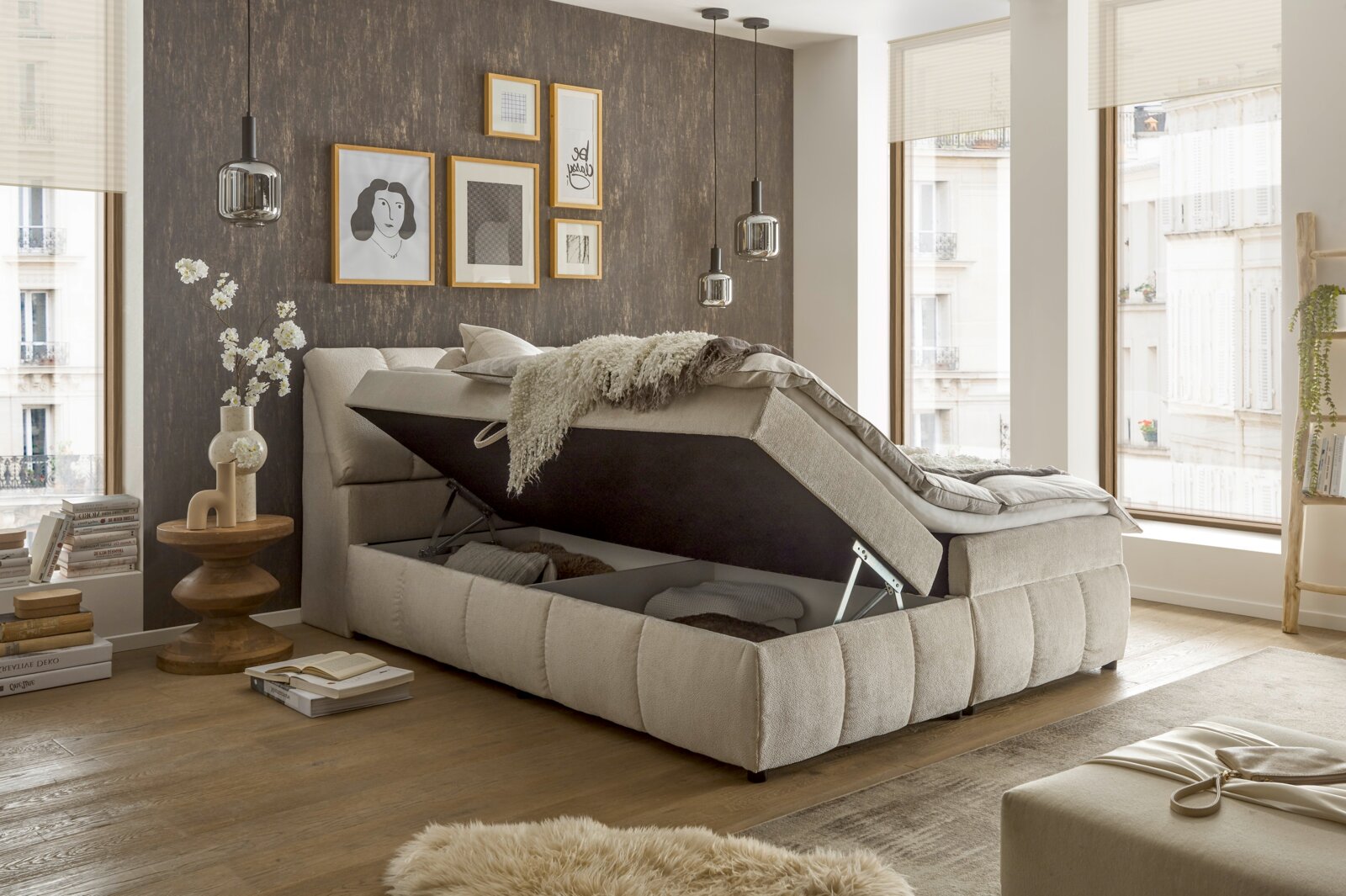 Boxspringbett VALENCIA mit Stauraum, seitliche Perspektive, in modernem Schlafzimmer mit dekorativer Wand und großen Fenstern.