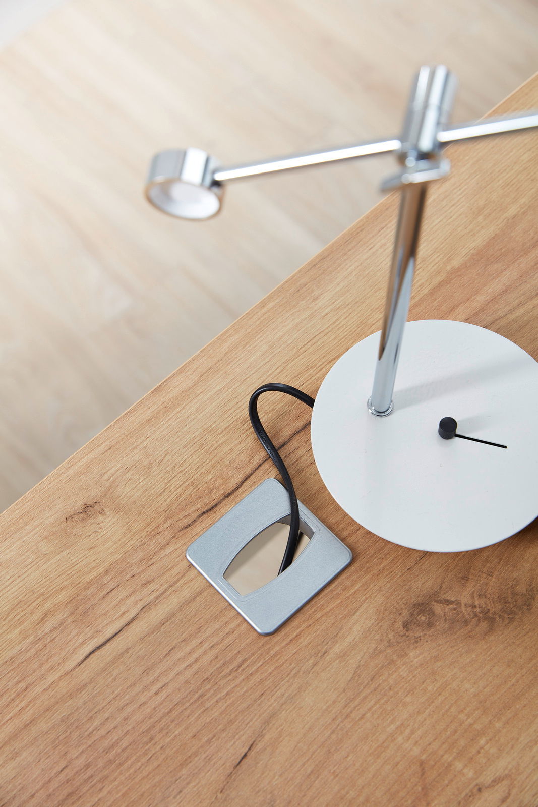 Nahaufnahme eines Schreibtischs mit einer modernen Tischlampe und einer Kabeldurchführung, aus der Vogelperspektive.