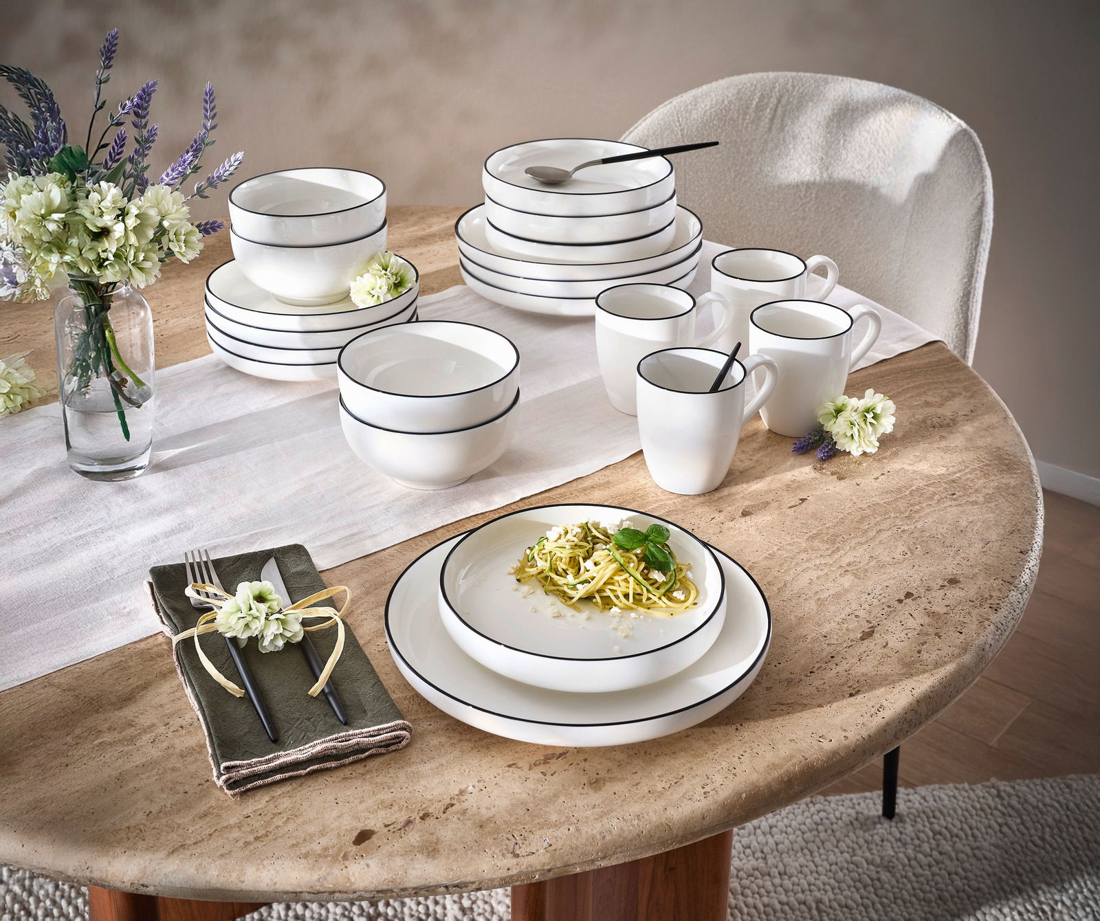 Novel Kombiservice 20-tlg. OSLO Kombiservice 20-tlg. auf einem Tisch, bestehend aus weißen Tellern, Schalen und Tassen mit schwarzem Rand, dekoriert mit Blumen und Besteck, seitliche Perspektive.