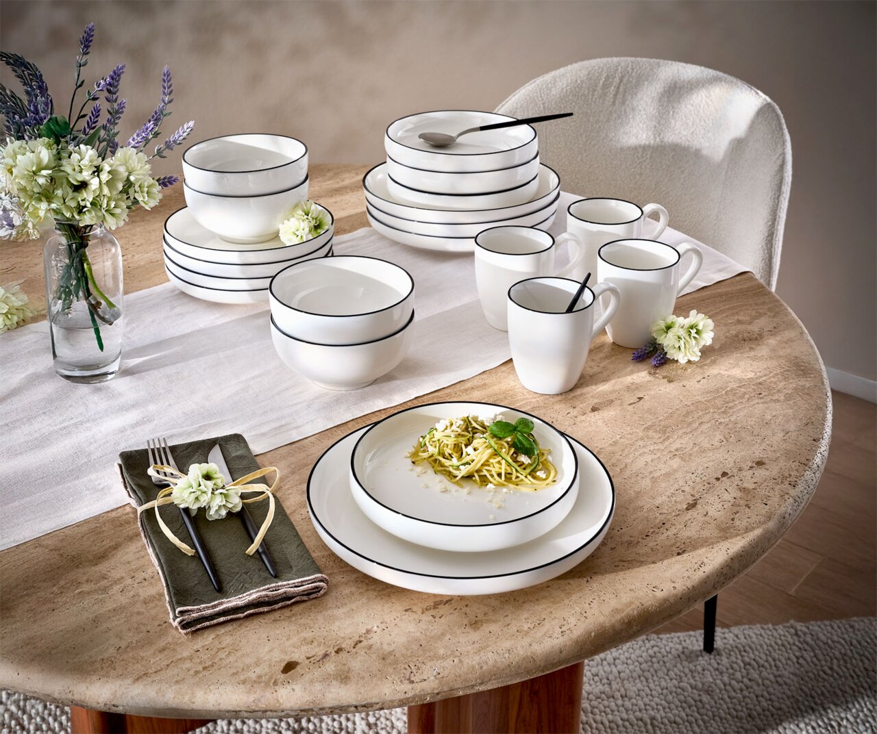 Servies set van 20 stuks op een tafel, bestaande uit witte borden, schalen en kopjes met een zwarte rand, versierd met bloemen en bestek, zijaanzicht.
