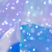 Nahaufnahme aus schräger Innenperspektive auf die Ecke einer transparenten Acrylbox mit blau-violettem Bokeh-Licht und sichtbarer Befestigung/Lasche.