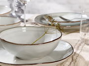 Nahaufnahme eines eleganten, elfenbeinfarbenen Frühstückssets mit braunem Rand, bestehend aus Schalen und Tellern, auf einem gedeckten Tisch.