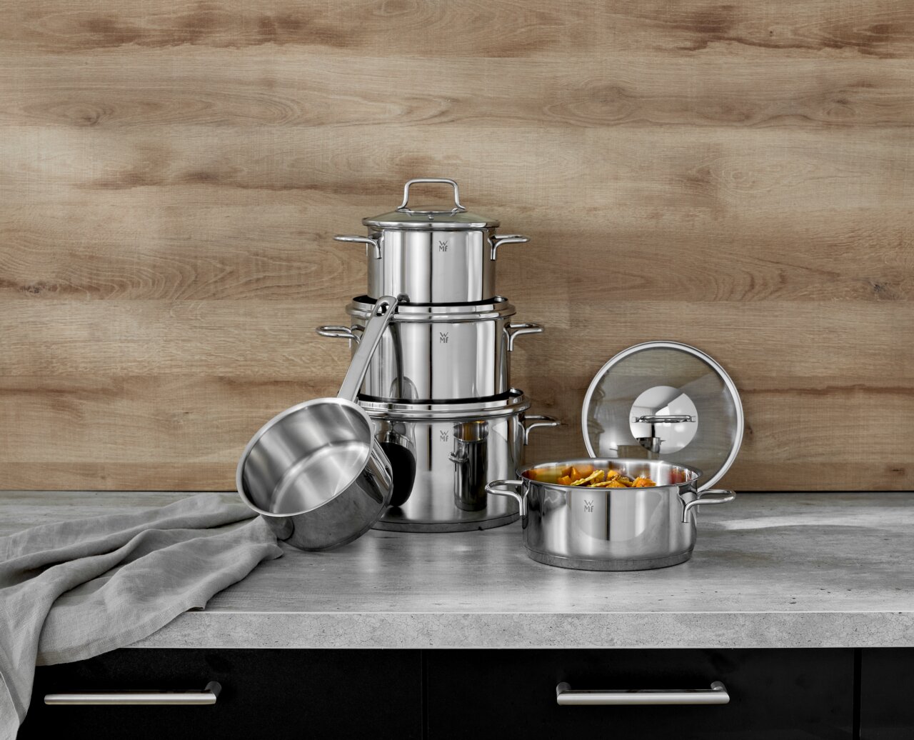 WMF Topfset 5-tlg. ASTORIA Topfset Astoria 5-tlg. aus Edelstahl, bestehend aus mehreren Töpfen und Deckeln, auf einer Küchenarbeitsplatte vor einer Holzrückwand, seitliche Perspektive.