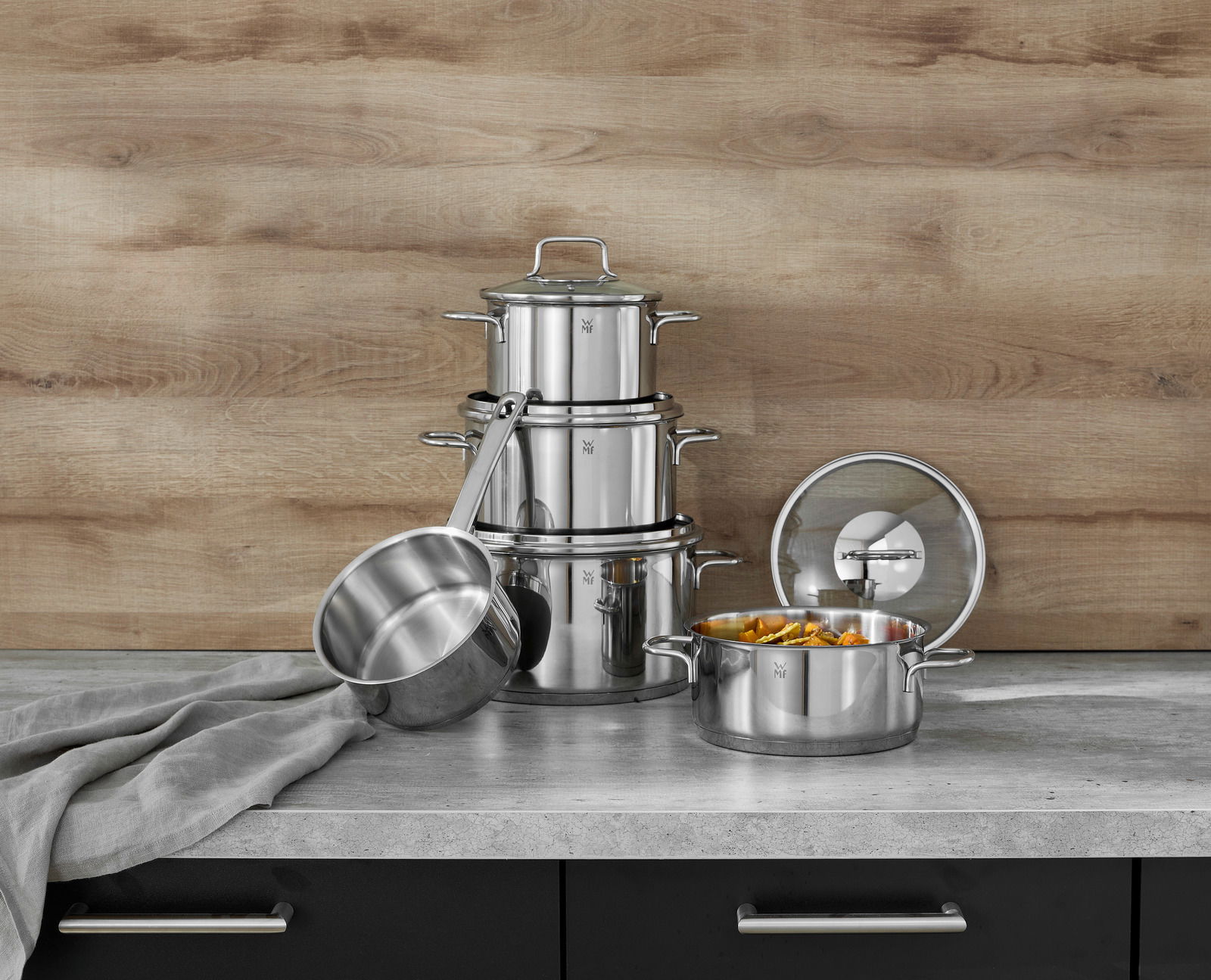 Topfset Astoria 5-tlg. aus Edelstahl, bestehend aus mehreren Töpfen und Deckeln, auf einer Küchenarbeitsplatte vor einer Holzrückwand, seitliche Perspektive.