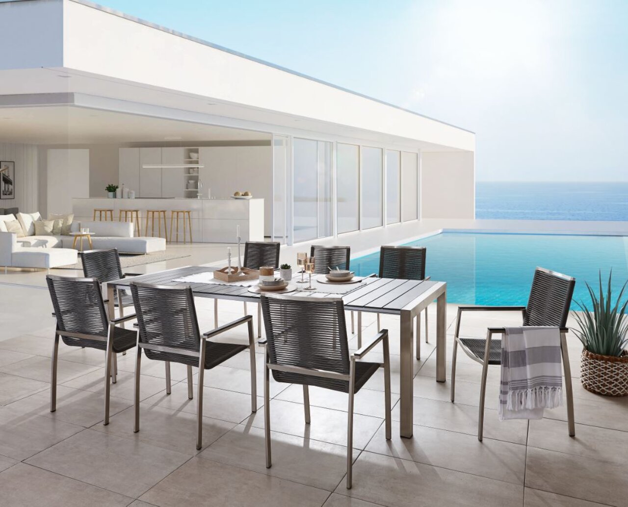 Amatio Uitschuifbare tafel GIRONA Een moderne uitschuiftafel op een terras met uitzicht op zee, omringd door stijlvolle stoelen, gefotografeerd vanuit een schuin bovenaanzicht.