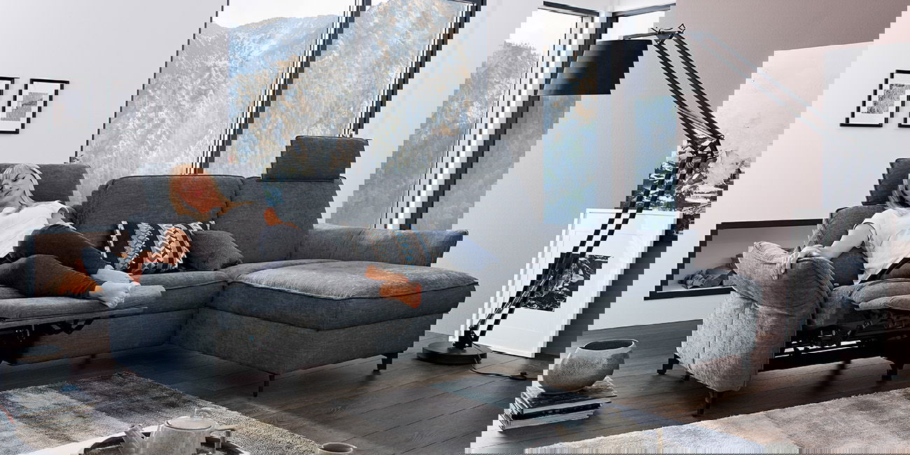 Ein graues Sofa mit Relaxfunktion. Eine Frau ruht sich aus.