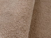 Nahaufnahme eines weichen, beigen Teppichs mit flauschiger Textur, perspektivisch von der Seite aufgenommen.