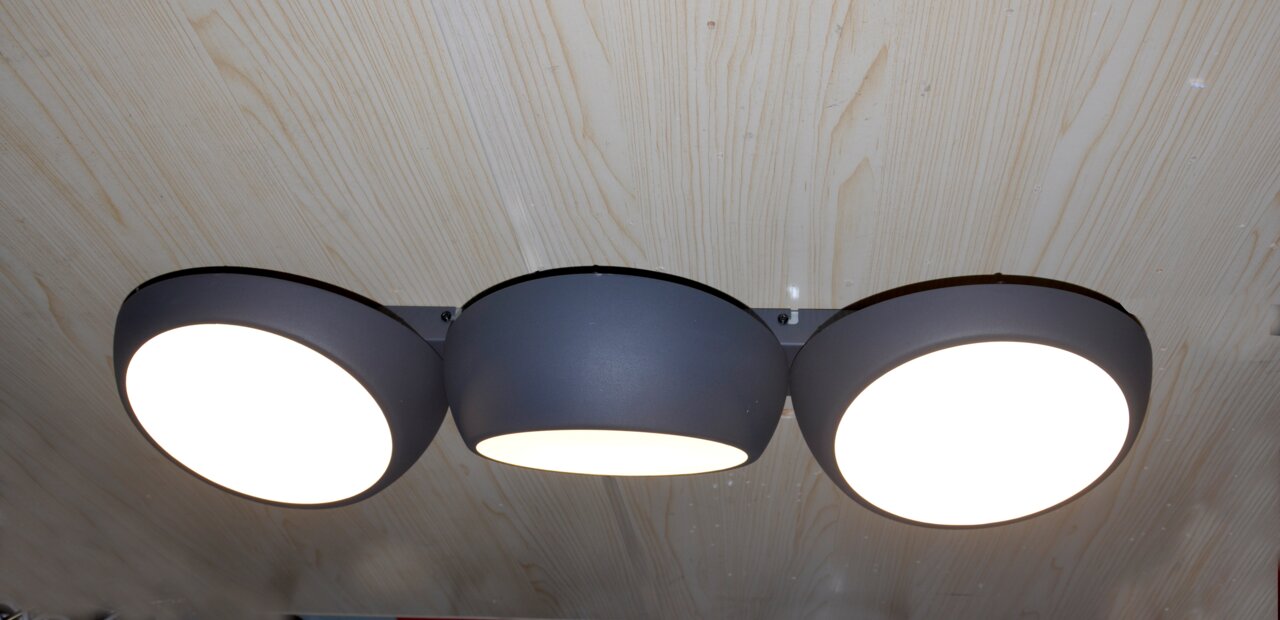 Novel LED-Deckenleuchte BUBBLES Moderne dreiflammige LED-Deckenleuchte in mattem Dunkelgrau mit drei runden, flachen Leuchtköpfen und opalen Diffusoren, warmweiß leuchtend, an Holzdecke montiert, Ansicht von unten (Untersicht).