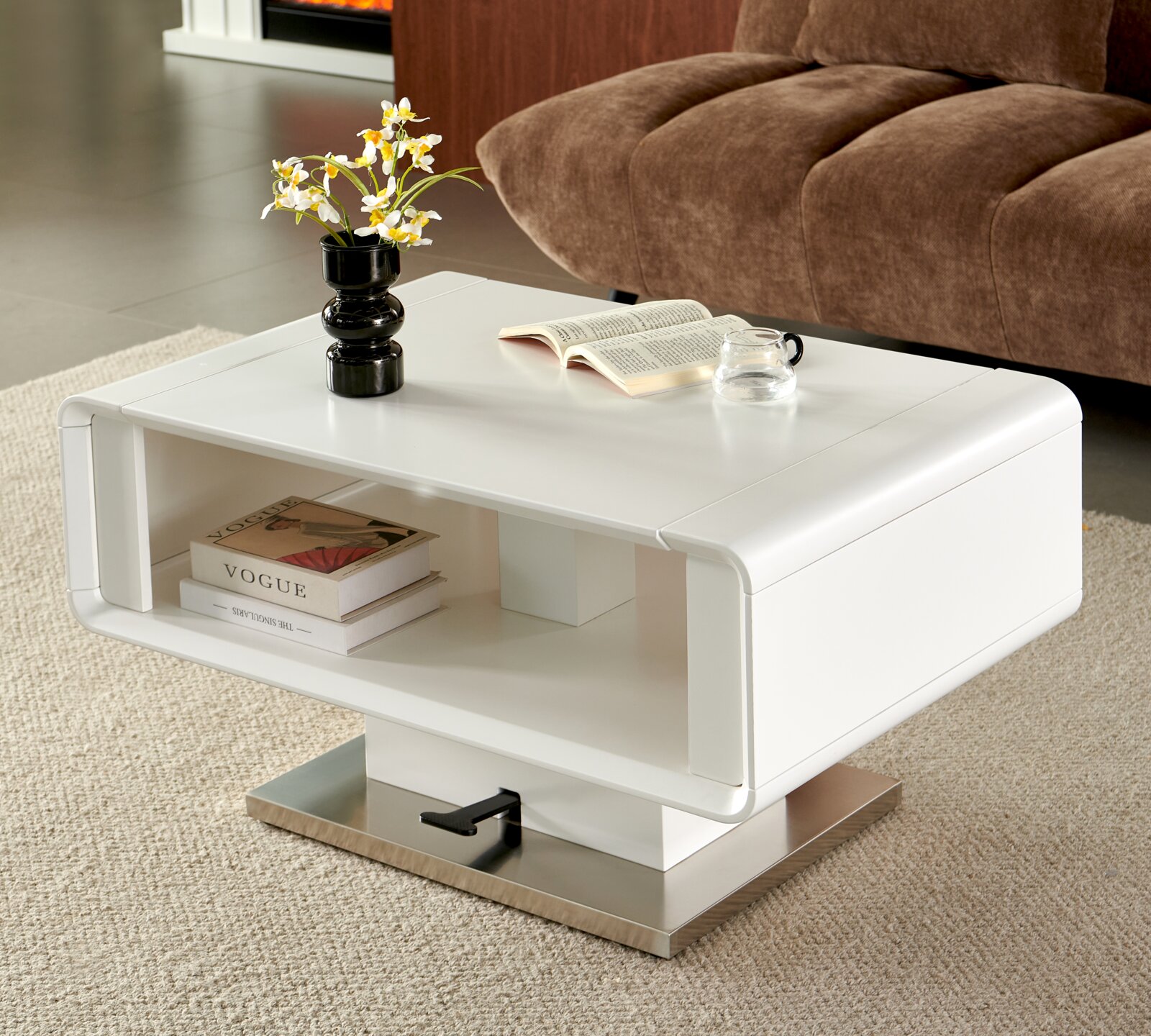 Witte moderne salontafel met afgeronde hoeken en open opbergnis op metalen voet, gestyled met vaas, boek en glas in een woonkamer; perspectief schuin van voren (driekwartaanzicht).