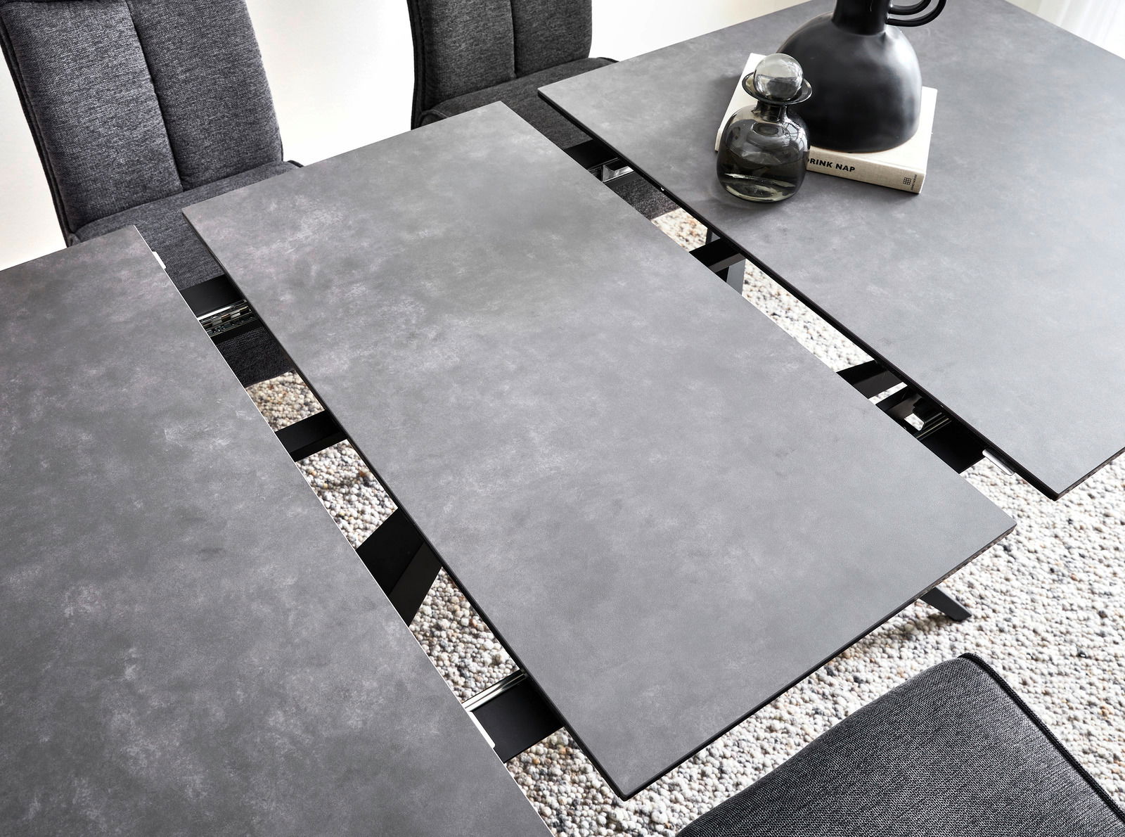 Moderner Esstisch mit grauer, erweiterbarer Tischplatte aus der Vogelperspektive, umgeben von grauen Stühlen.