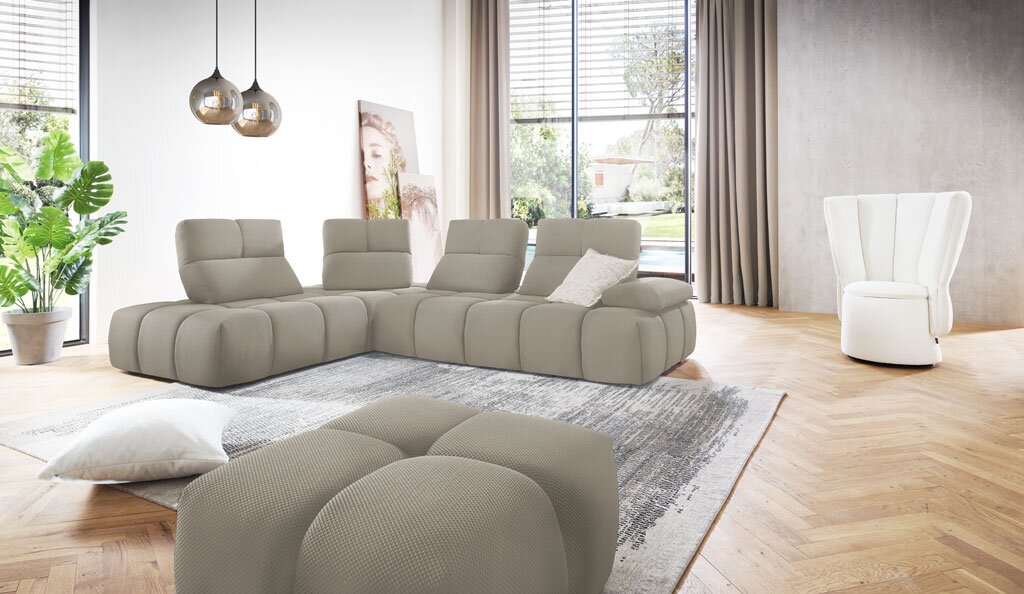 Modernes, hellgraues L-förmiges Modul-Ecksofa mit gepolsterten Rückenlehnen und Ottomane in einem hellen Wohnzimmer, aufgenommen in leichter Frontalansicht aus Augenhöhe.
