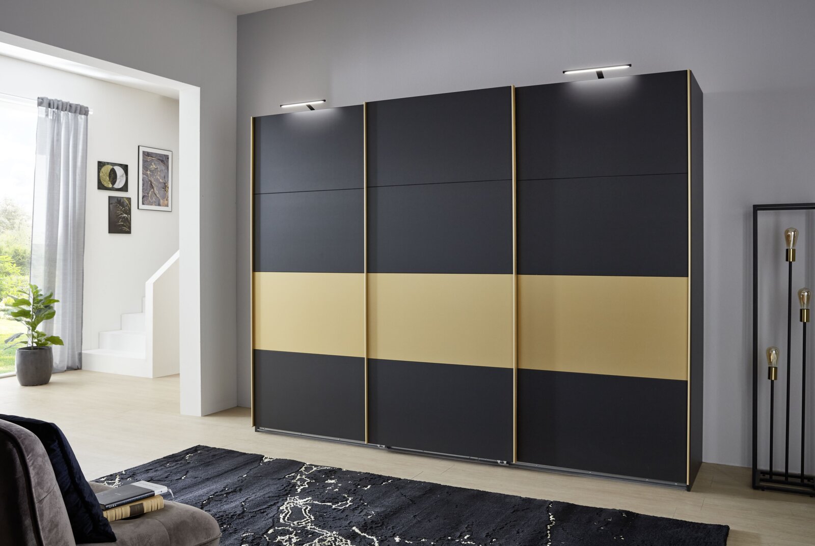 Z2 Hangende kast met 3 deuren DUBAI Moderner dreitüriger Schwebetürenschrank in Schwarz und Gold, frontal fotografiert in einem stilvoll eingerichteten Raum.