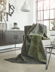 Gemütliche grüne Jacquard-Decke 150x200 cm auf einem Sessel in modernem Wohnzimmer, seitliche Perspektive.