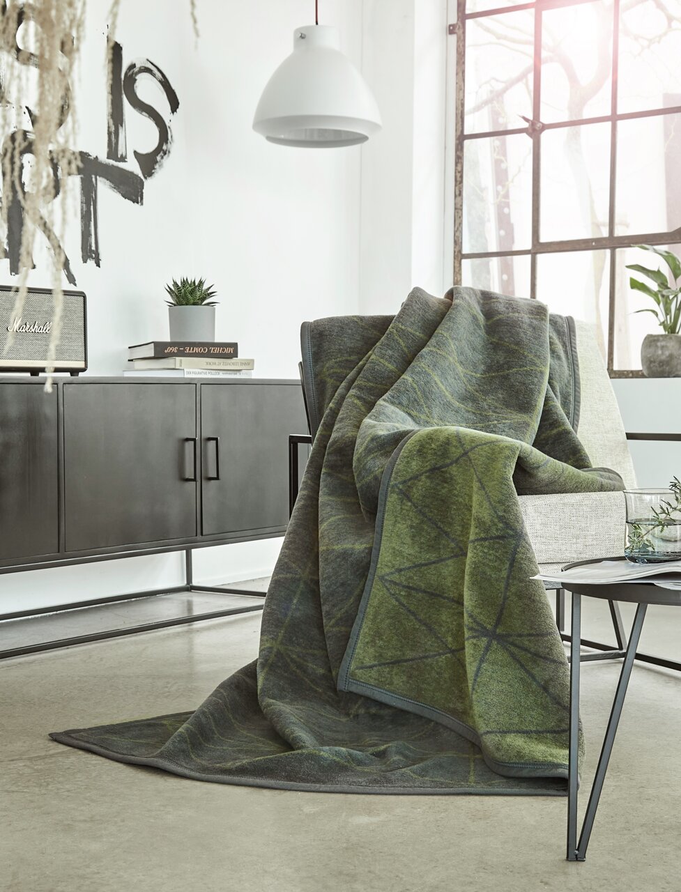 Gemütliche grüne Jacquard-Decke 150x200 cm auf einem Sessel in modernem Wohnzimmer, seitliche Perspektive.