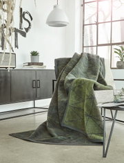Gemütliche grüne Jacquard-Decke 150x200 cm auf einem Sessel in modernem Wohnzimmer, seitliche Perspektive.