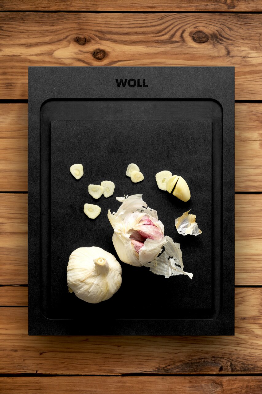 Schwarzes Schneidebrett mit Knoblauch, von oben fotografiert, auf einer Holzoberfläche.