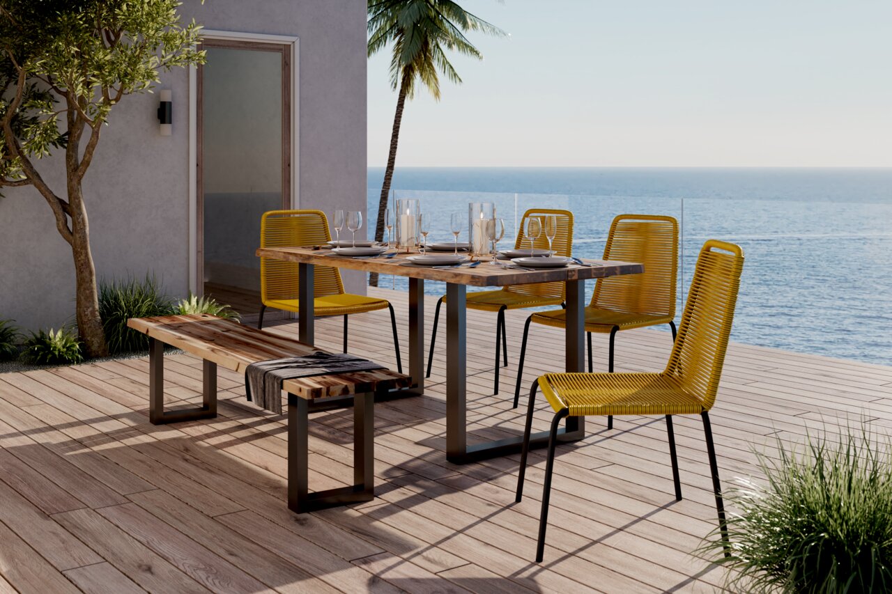 Gelber Stapelstuhl auf einer Terrasse mit Meerblick, neben einem Holztisch und einer Bank, seitliche Perspektive.