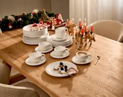 Ein festlich gedeckter Tisch mit einem 12-teiligen Dinner-Set, bestehend aus weißen Tellern und Tassen, dekoriert mit weihnachtlichen Elementen wie Kerzen und Rentierfiguren. Perspektive von oben.