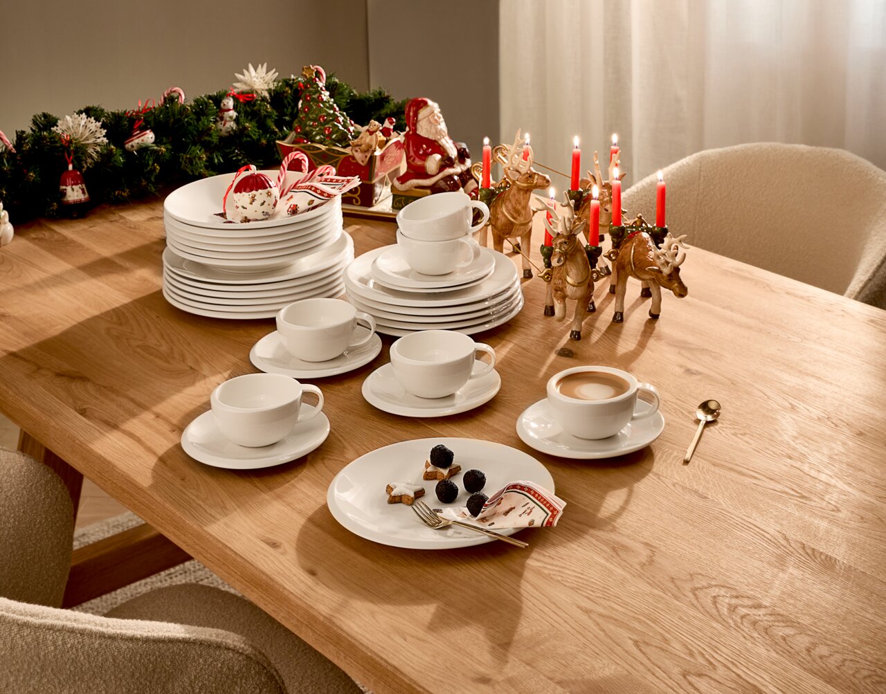 Ein festlich gedeckter Tisch mit einem 12-teiligen Dinner-Set, bestehend aus weißen Tellern und Tassen, dekoriert mit weihnachtlichen Elementen wie Kerzen und Rentierfiguren. Perspektive von oben.