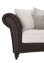 Nahaufnahme eines Megasofas mit brauner Lederoptik und Nietenverzierung, helle Kissen, seitliche Perspektive