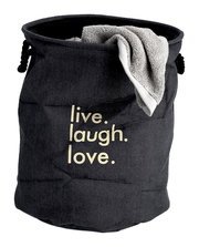 Wäschesammler 'Denim' in dunkler Jeansoptik mit dem Aufdruck 'live. laugh. love.' und einem Handtuch, aus der Vorderansicht fotografiert.