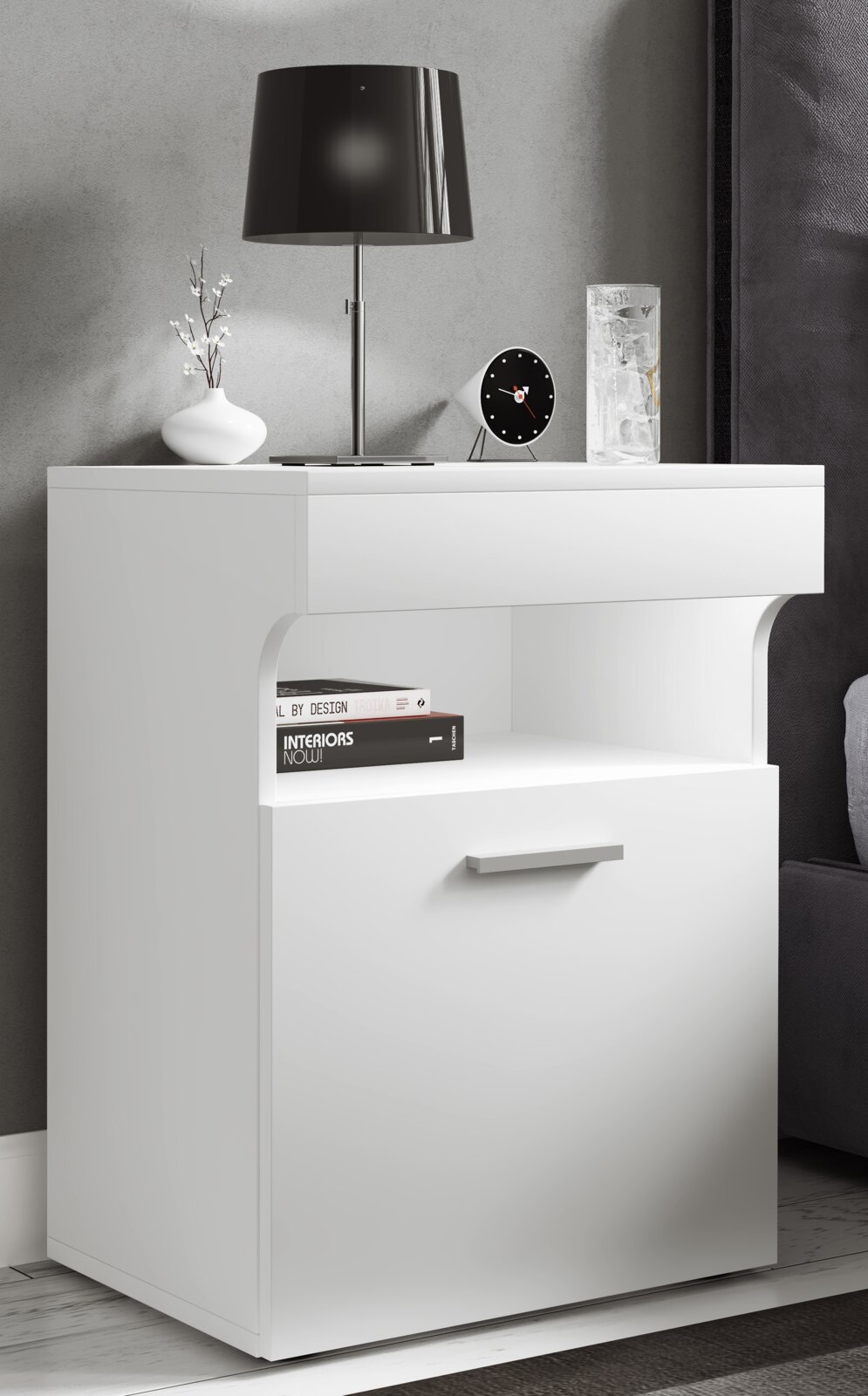 Weißer moderner Nachttisch/Beistellschrank mit offener Ablage und Schublade, auf der Oberfläche eine schwarze Tischlampe und Deko, frontal in leichter Seitenperspektive fotografiert.