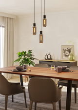 Moderne Pendelleuchte mit drei hängenden Glühbirnen über einem Esstisch, seitliche Perspektive.