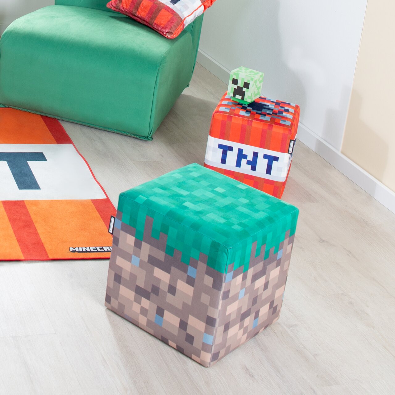 Minecraft Sitzwürfel im Grasblock-Design in einem hellen Zimmer, Vorderansicht leicht von oben; im Hintergrund ein TNT-Würfel und ein grüner Sessel.