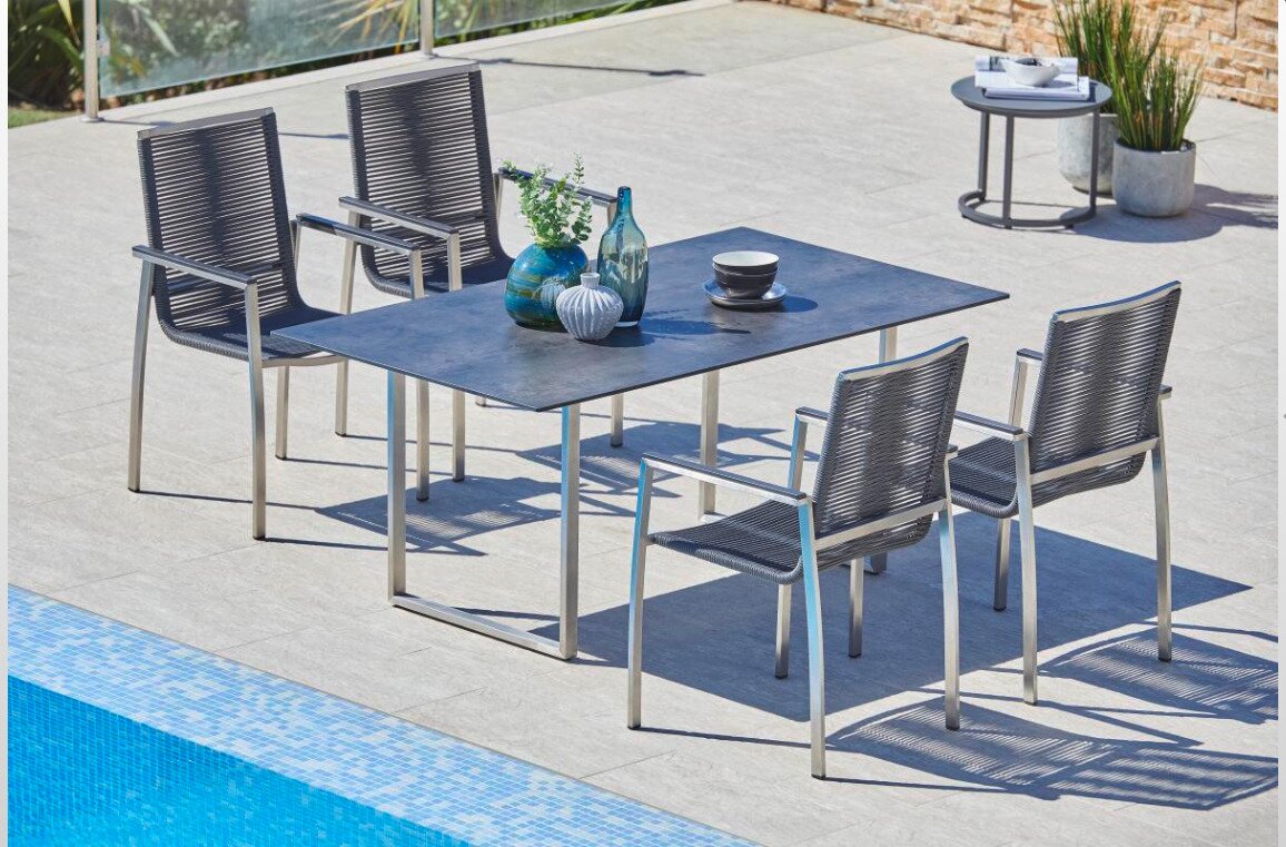 Moderne Gartenmöbelgarnitur mit Tisch und vier Stühlen aus Metall und Kunststoffgeflecht, seitliche Perspektive am Pool.