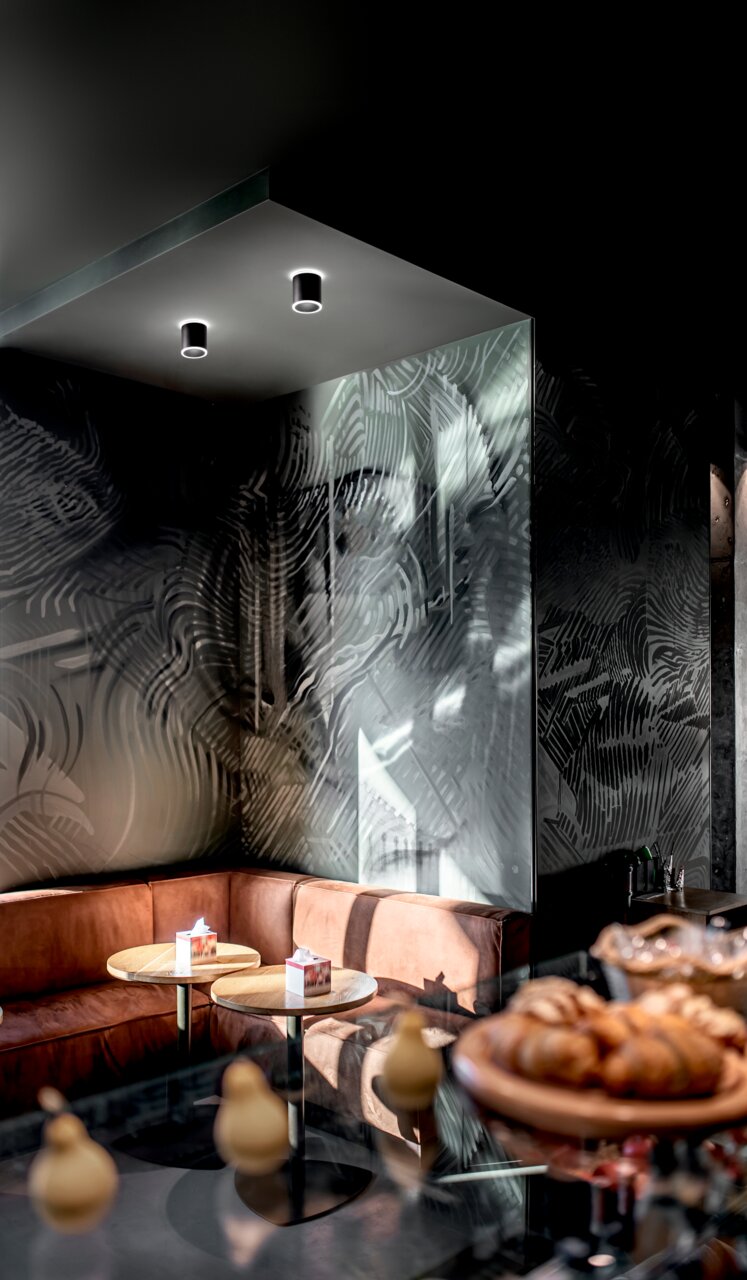 Fabas Luce LED-Aufbauspot PACA Zwei schwarze LED-Aufbauspots an der Decke eines stilvoll eingerichteten Cafés, Perspektive von unten.