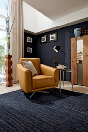 Moderne draaifauteuil in mosterdgeel, gezien vanaf de zijkant, in een stijlvol ingerichte woonkamer met donkere muren en houten meubels.