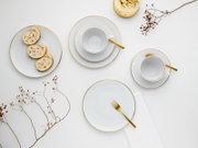 Draufsicht auf elegantes weißes Porzellan-Geschirrset mit feiner Goldkante, zwei Tassen auf Untertassen, Teller mit Biskuitrollen und goldfarbenem Besteck auf hellem Hintergrund