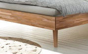 Close-up van een houten bedframe met natuurlijke nerf, gefotografeerd vanaf de zijkant.