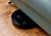 Ein Saugroboter, der unter einem Sofa auf einem Holzboden reinigt. Perspektive von oben.