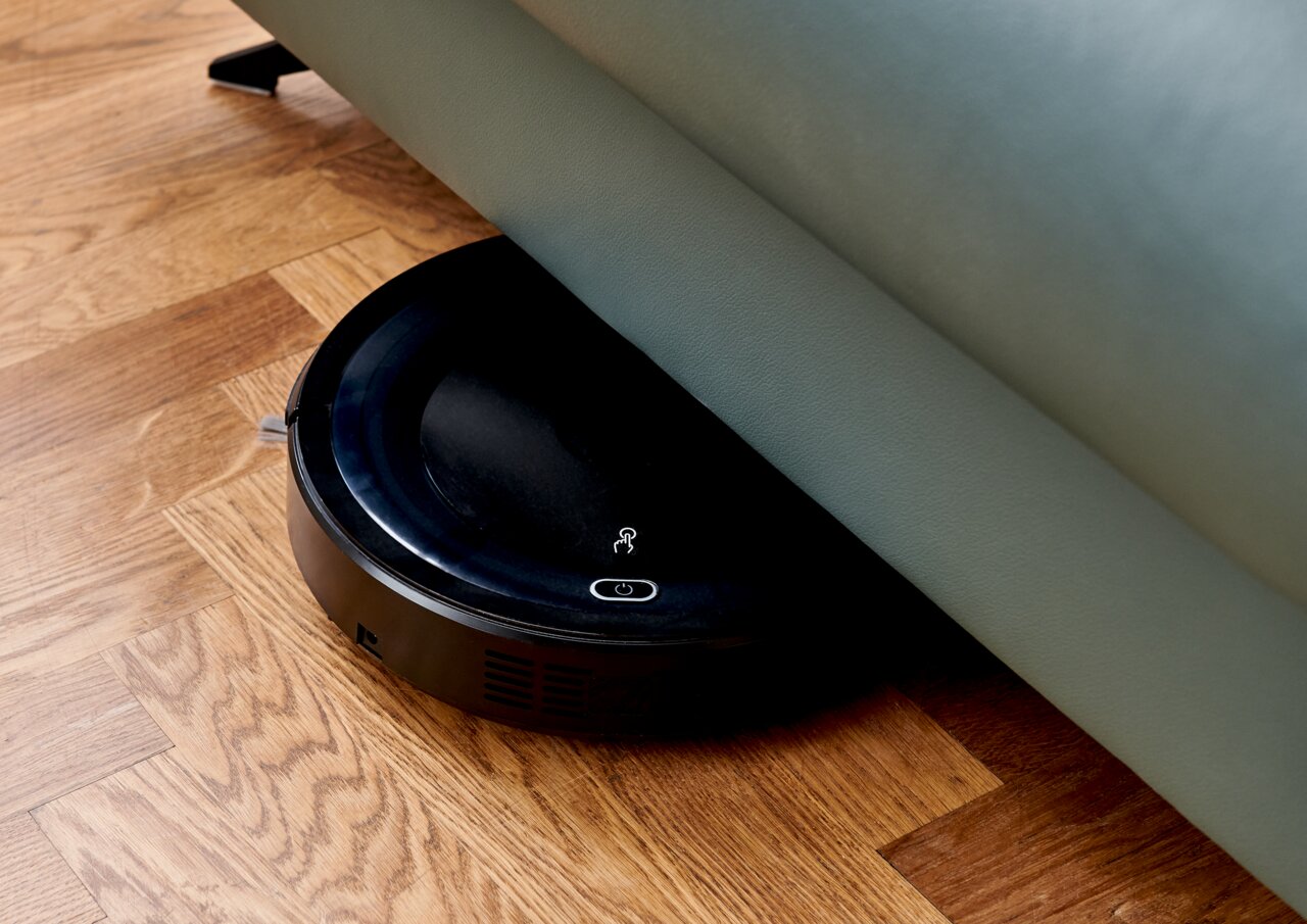 Ein Saugroboter, der unter einem Sofa auf einem Holzboden reinigt. Perspektive von oben.