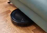Ein Saugroboter, der unter einem Sofa auf einem Holzboden reinigt. Perspektive von oben.