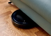 Ein Saugroboter, der unter einem Sofa auf einem Holzboden reinigt. Perspektive von oben.