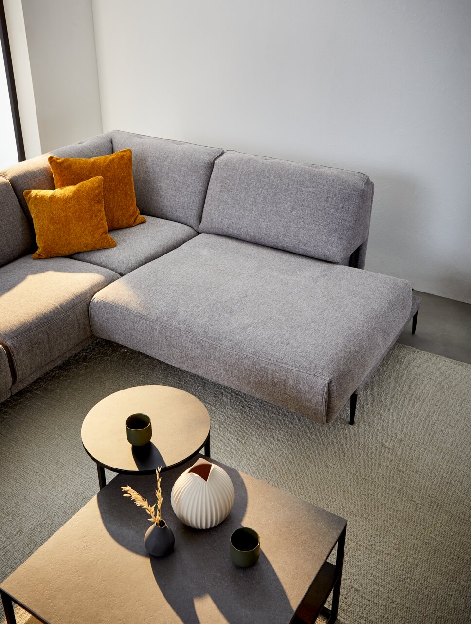 Graue Polsterrundecke mit zwei senfgelben Kissen, fotografiert aus der Vogelperspektive, neben zwei runden Beistelltischen mit Dekoration.