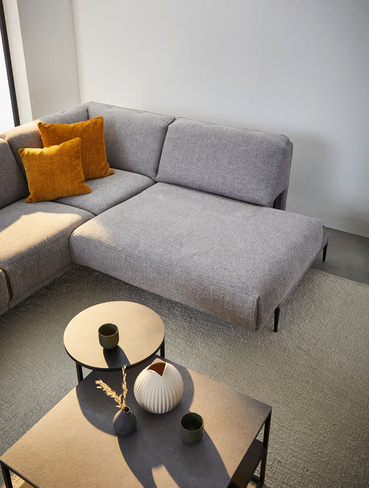 Graue Polsterrundecke mit zwei senfgelben Kissen, fotografiert aus der Vogelperspektive, neben zwei runden Beistelltischen mit Dekoration.
